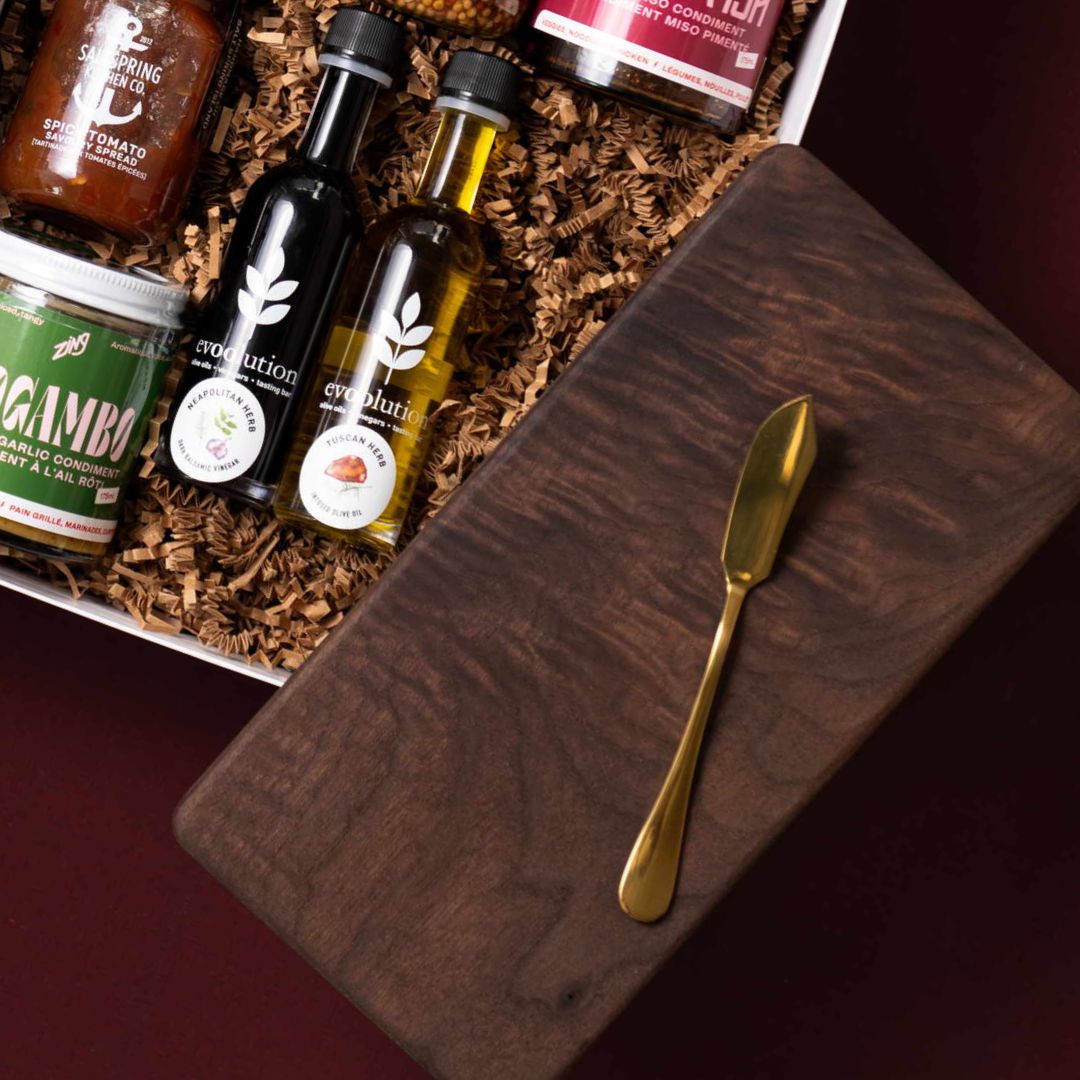 Handmade walnut board and gold butter knife beside Evoolution oils and gourmet condiments.
